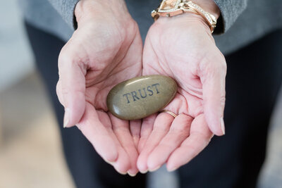 Tammy holding a smooth rock with the word "Trust" engraved into it.