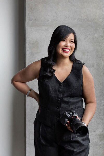 Woman sitting down with a camera on her hands while posing for a portrait.