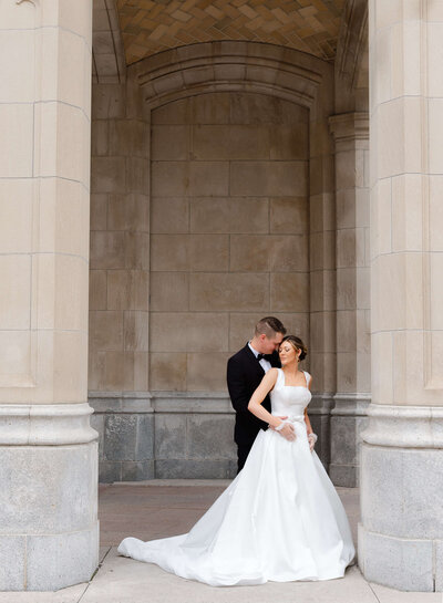 Ottawa wedding photography of a groom in a black suit hugging his bride in a white ballgown.  Captured outdoors at the Chateau Laurier wedding venue in Ottawa by Ottawa wedding photographer JEMMAN Photography