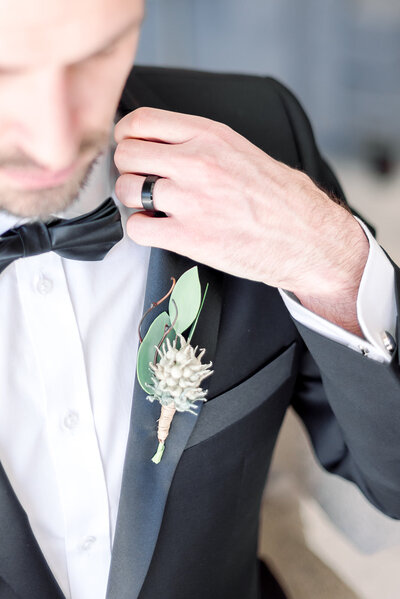 groom holding onto his lapel while showing off his boutonniere and wedding band getting ready for a classic Colorado photography look