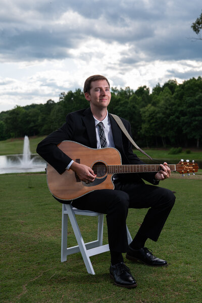 A person sitting on a chair in a field with a guitar 