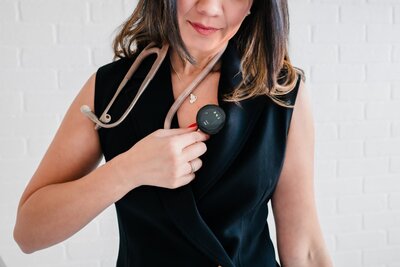 Close-up of cardiologist in black pantsuit holding stethoscope to heart during San Antonio studio branding session.