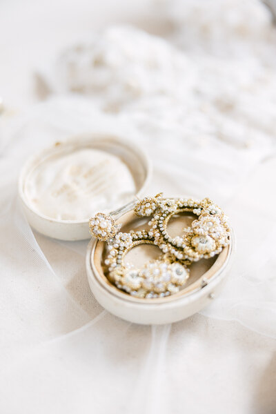A delicate pair of handcrafted pearl and gold bridal earrings elegantly displayed in a vintage jewelry box. Captured during a luxury wedding at the Dewberry Hotel in Charleston by Amia Marcell Photography.