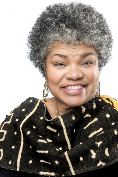 black woman with salt and pepper afro wearing mud cloth smiling at camera headshot