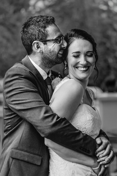 Black and white images of the Groom holding his arms around his bride while whispering into her ear. She giggles beautifully. 