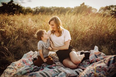 A mother and her son in a field of tall grass captured during our family photography session. Theta re sitting on a patchwork multicolor blanket, creating a scene of pure joy.