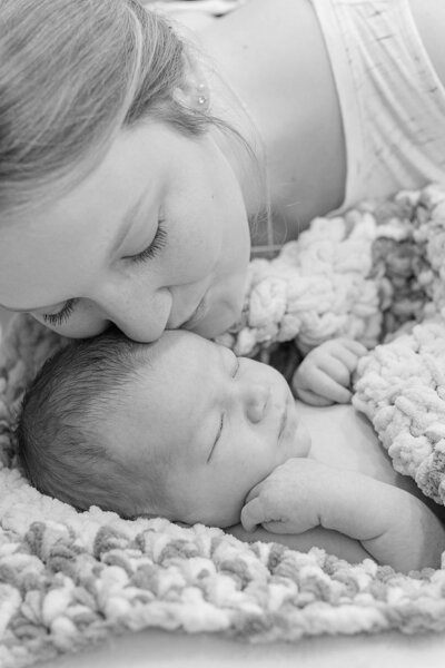 Black and white image of mom kissing newborn baby on forehead