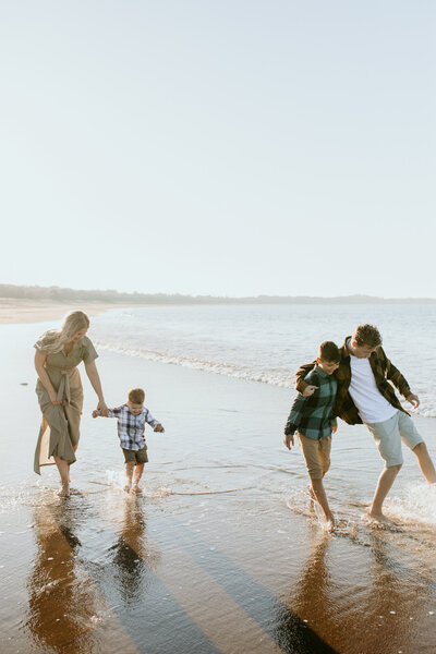 Family of four enjoying a beach walk, kicking water under the warm glow of the setting sun.