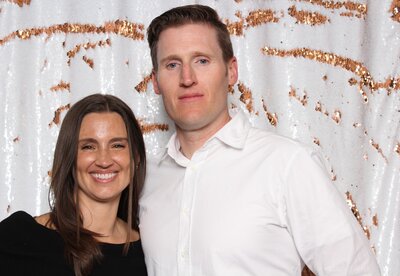 Couple smiling in front of white and gold backdrop for photo booth