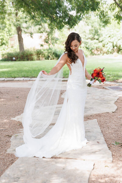 Bride twirls her veil while holding a bold red-orange bouquet, enjoying a joyful wedding day planned in the Austin Hill Country.