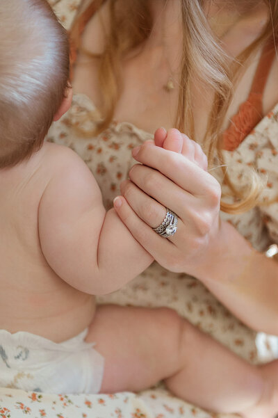 Close-up of a mother’s hands gently holding her newborn’s tiny hands.