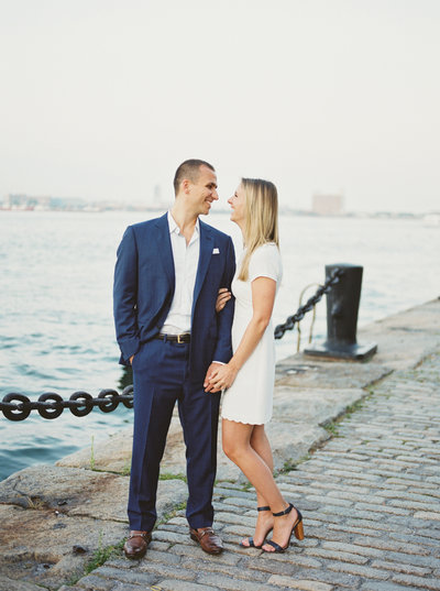newly engaged couple wearing blue suit and white dress at waterside engagement session