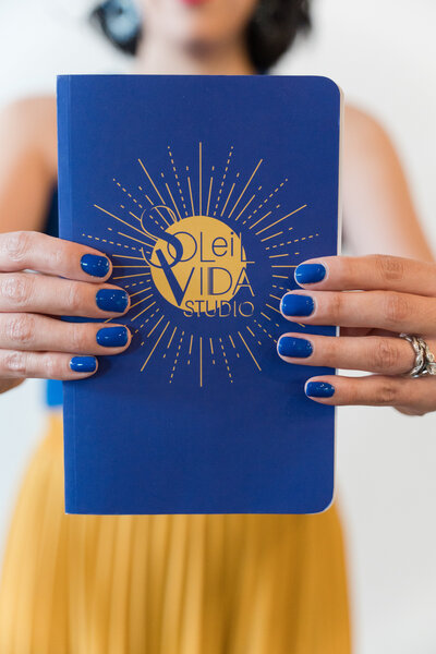 The artful world guided by our founder! Witness her expertise as she holds a branded agenda with the yellow submark logo in both hands. Adorned in a vibrant blue top, a yellow skirt, and showcasing brand-coordinated blue nails.