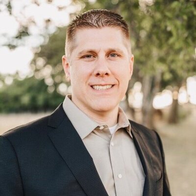 brian burzynski in a black suit coat with trees in the background