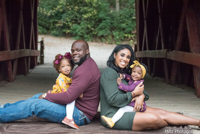 A family of four posing outdoors smiling at the camera photographed by Millz Photography in Greenville, SC