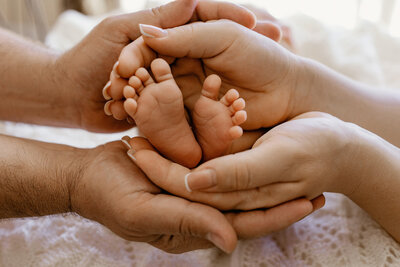 Close-up of newborn baby feet gently cradled in both parents' hands — captured during an in-home newborn session in Las Vegas by Angela Wolf Photography