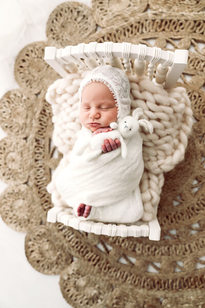Newborn bliss: a serene baby sleeps soundly swaddled in white, cradled on a lacey background with a plush bunny by their side. Taken by Fig and Olive Photography, a Twin Cities Newborn Photographer