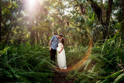 couple kissing surrounded by ferns  at pregnancy photoshoot