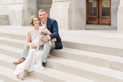 married couple dressed up and sitting on stairs in downtown Kansas City holding their small dog