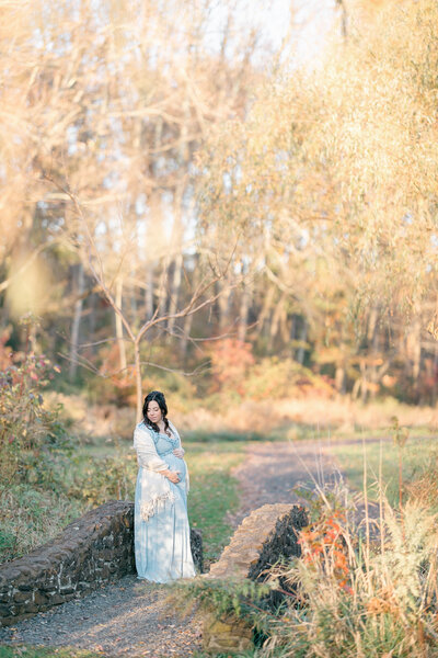 Pregnant woman cradling her bump on bridge in the fall by  NJ maternity Photographer