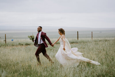 bride and groom holding hands running in field