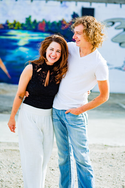 A engaged couple laughing in front of a mural in Toledo Ohio