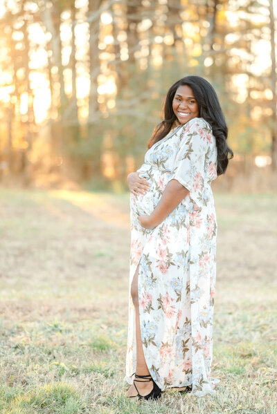 Mom to be in white dress  with flowers smiles big during her maternity session with Justine Renee Photography.