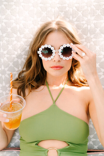 woman sitting poolside with daisy sunglasses