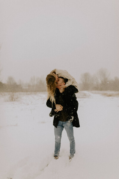 A woman sitting on her boyfriend's  shoulders outside while it's snowing