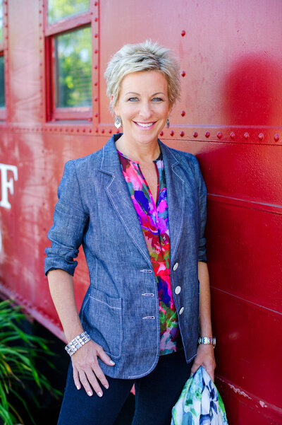 Headshot of Julianne Stitick posing by a red caboose during her brand photography session wearing a denim blazer.