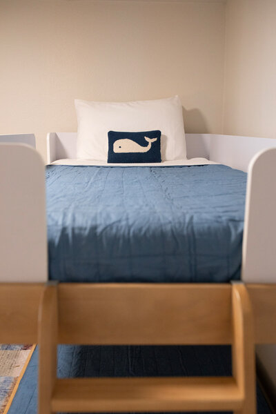 Bunk bed details from a short term rental renovation featuring a blue duvet cover and a pillow with a whale motif.