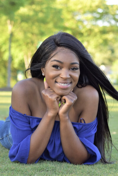 a senior laying in the grass posing with her hands on her chin. photographed by Millz Photography in Greenville, SC