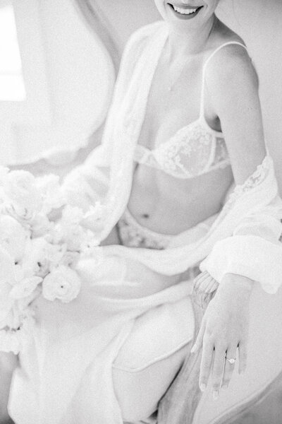 Bride in her lingerie and robe sitting in a chair smiling