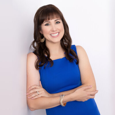Headshot of Brittany Hodak, customer experience keynote speaker. She wears a blue dress and is leaning against the wall with her arms crossed.