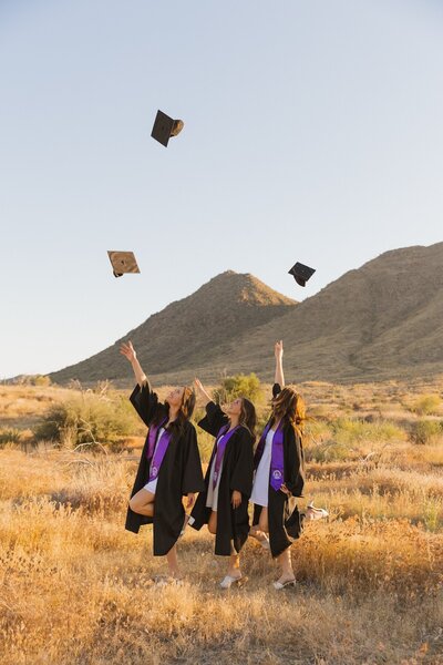 three girls toss up graduation caps for photoshoot in arizona desert