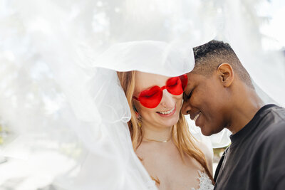 Lesbians having a tender moment under a veil during their Destination Elopement