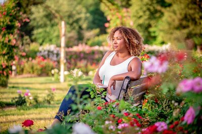 woman on bench in a rose garden gazing in the distance holding a iced black coffee