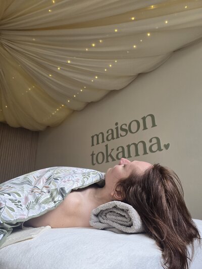 Cliente installée dans le lit de massage chez Maison Tokama à Rennes, sous une tenture lumineuse et apaisante au plafond.