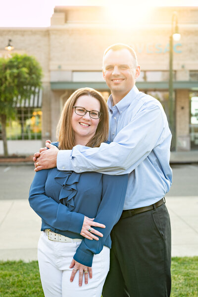 A husband and wife in an embrace smile at the camera  for their family photos in downtown Huntsville Alabama
