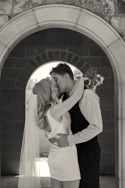 Black and white image of bride and groom holding each other and kissing.
