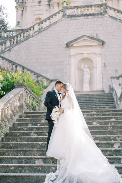 Romantic couple embracing on stone stairs with cathedral in background, timeless wedding photo near Toronto
