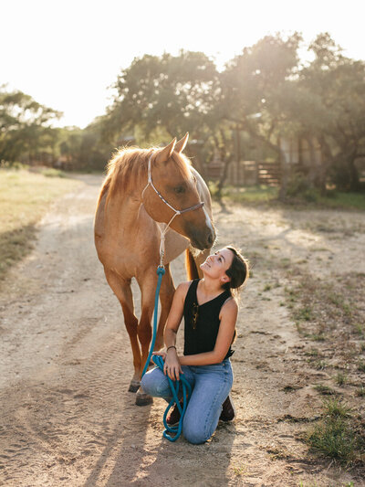 Girl looks up at her red roan horse at sunset