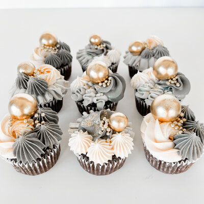 Chocolate cupcakes frosted with pink and grey frosting. Cupcakes are decorated with gold balls and sprinkles.