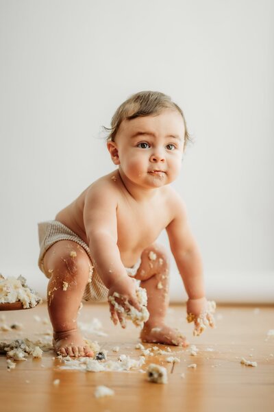 messy toddler standing over his smashed cake in a photography studio