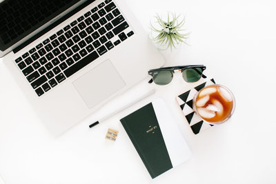 flat lay in black and white on desk with laptop, pen,  note book and sun glasses