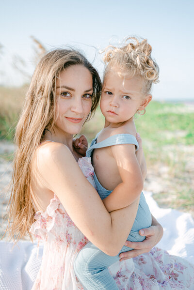 A mom and her baby at the beach looking at the camera