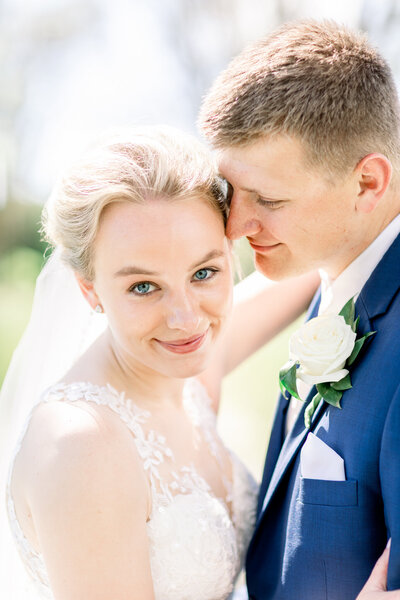 Close up of a groom in a blue suit sweetly nuzzling his bride as she smiles at their Wisconsin wedding photographer