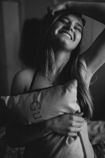 woman holding pillow and laughing during boudoir photoshoot
