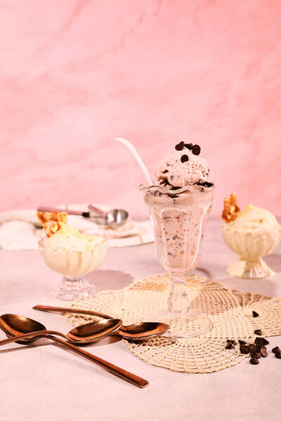 A playful and inviting image of ice cream sundaes topped with chocolate chips and served in glass dishes against a pink backdrop. Captured by Austin-based photographer Mica McCook, this image highlights the creamy textures and indulgent toppings.