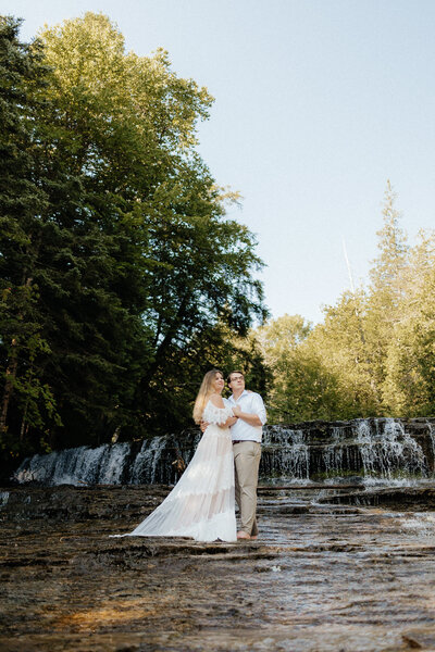 bride and groom standing together with a waterfall in the background and green trees